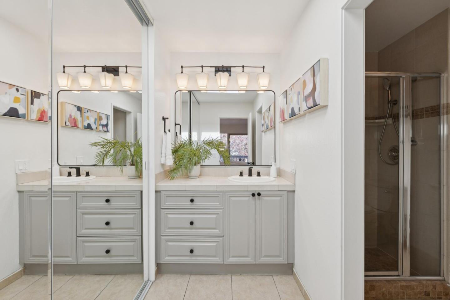 Bright bathroom with a white double vanity, large mirrors, and a glass-enclosed tiled shower.