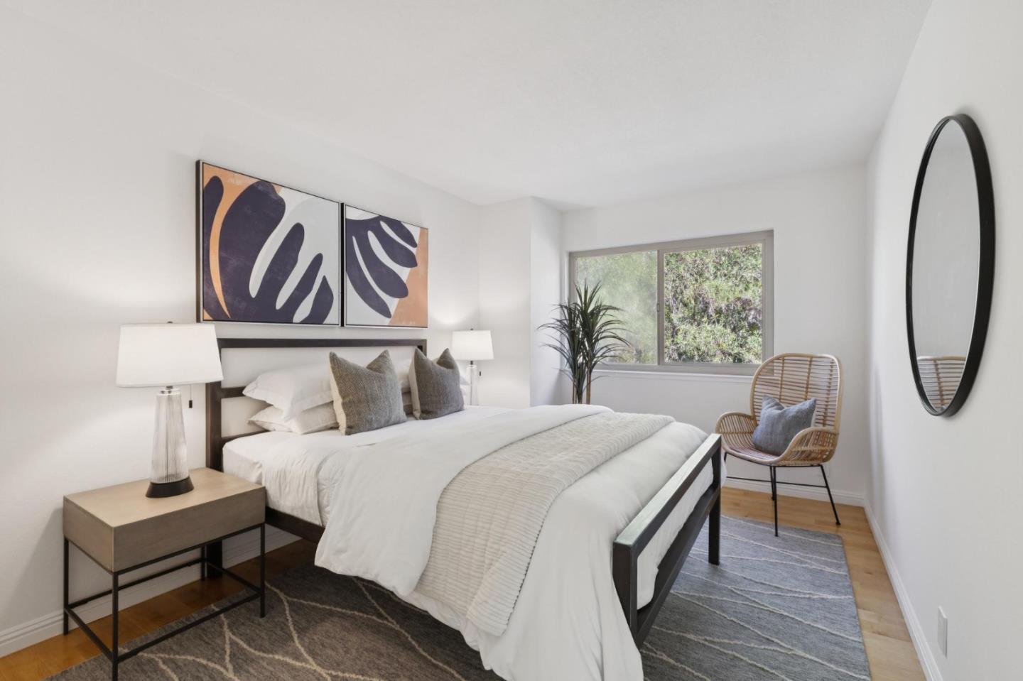 Staged bedroom with white bedding, abstract artwork, and a wicker chair beside the window.