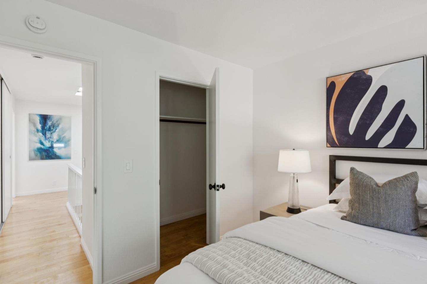 Bedroom with white bedding, abstract wall art, and an open closet beside the hallway.
