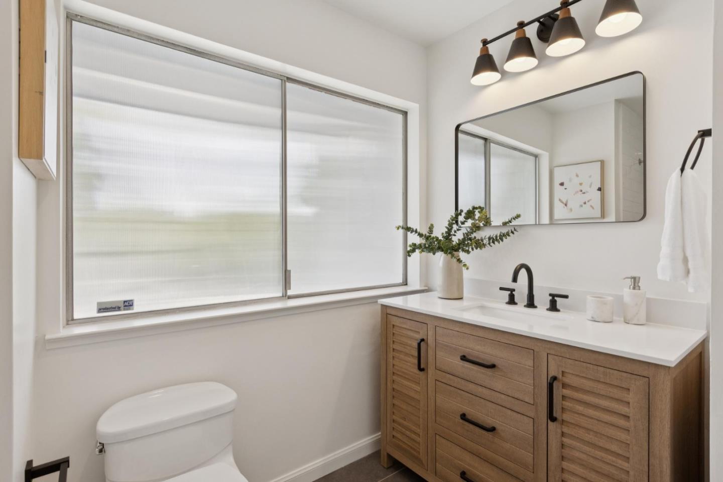 Bathroom with a wood vanity, black faucet, large shaded window, and toilet.