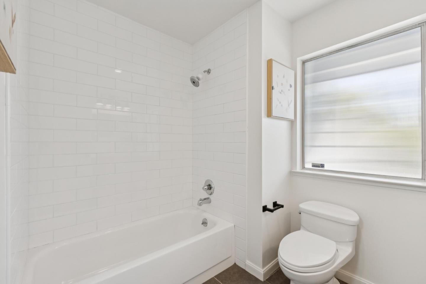 Bathroom with a white subway-tile tub and shower beside a toilet and large window.