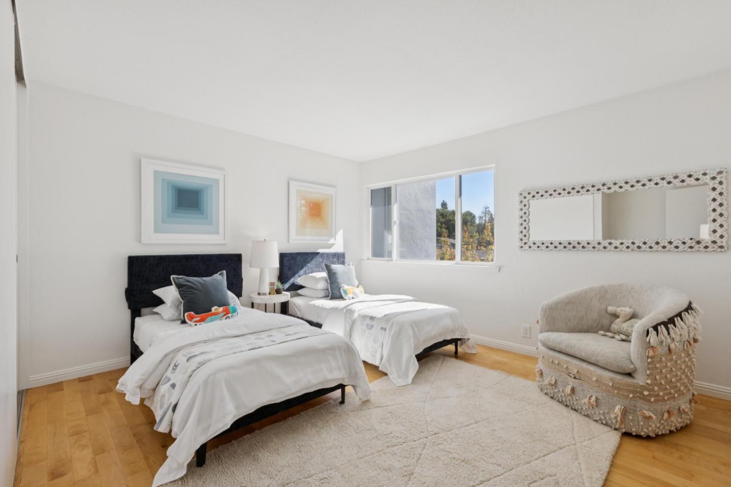 Bedroom with two twin beds, white bedding, a large window, and a cream accent chair.