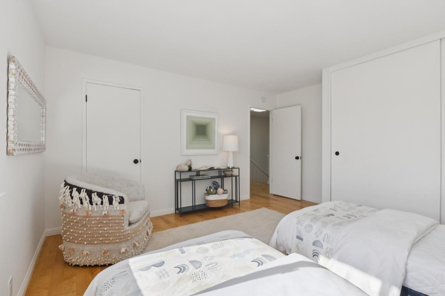 Bedroom with two beds, a textured accent chair, hardwood flooring, and white closet doors.