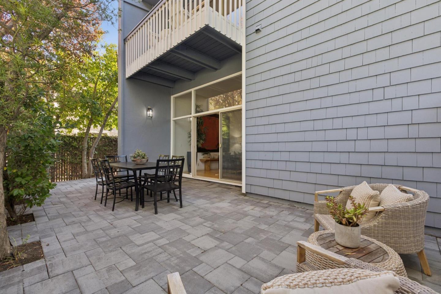 Paved patio with a black dining set, wicker lounge chairs, and sliding glass doors.
