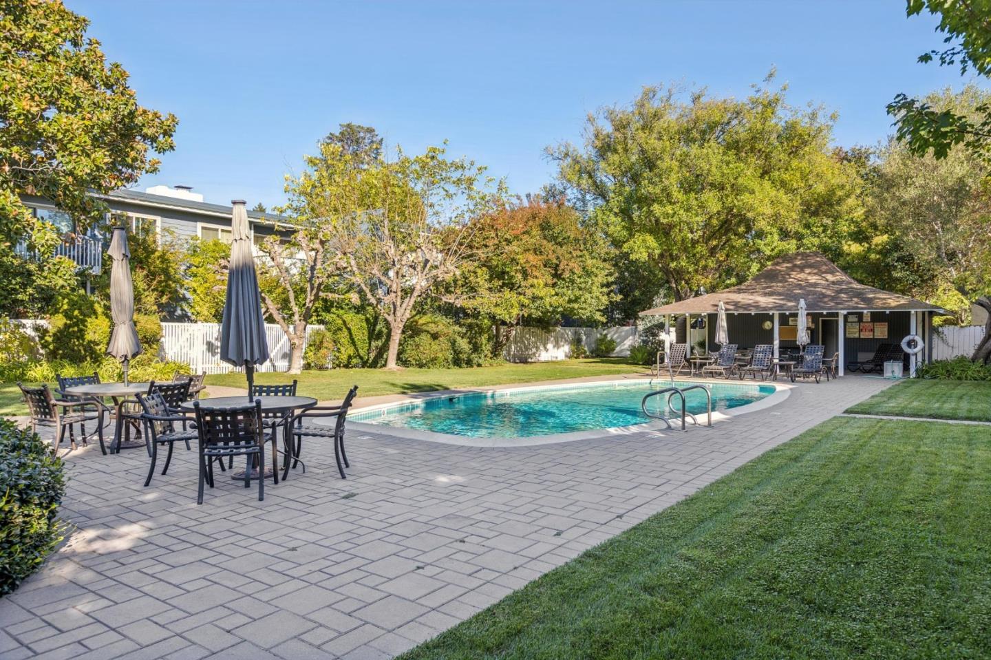 Outdoor pool with a paved patio, lawn, and covered poolside seating area.