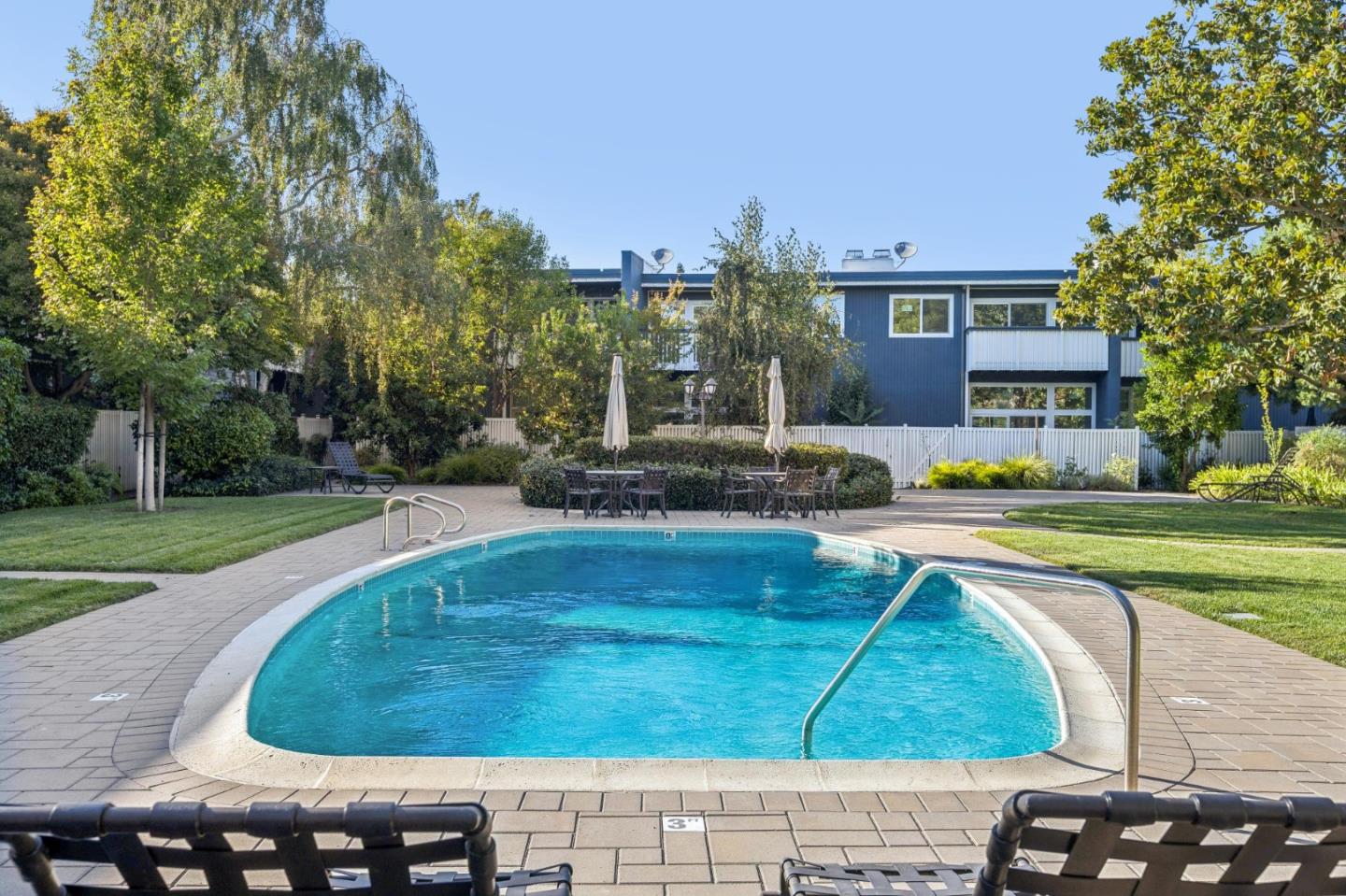 Outdoor swimming pool with curved entry steps, lounge chairs, and a blue two-story building behind it.