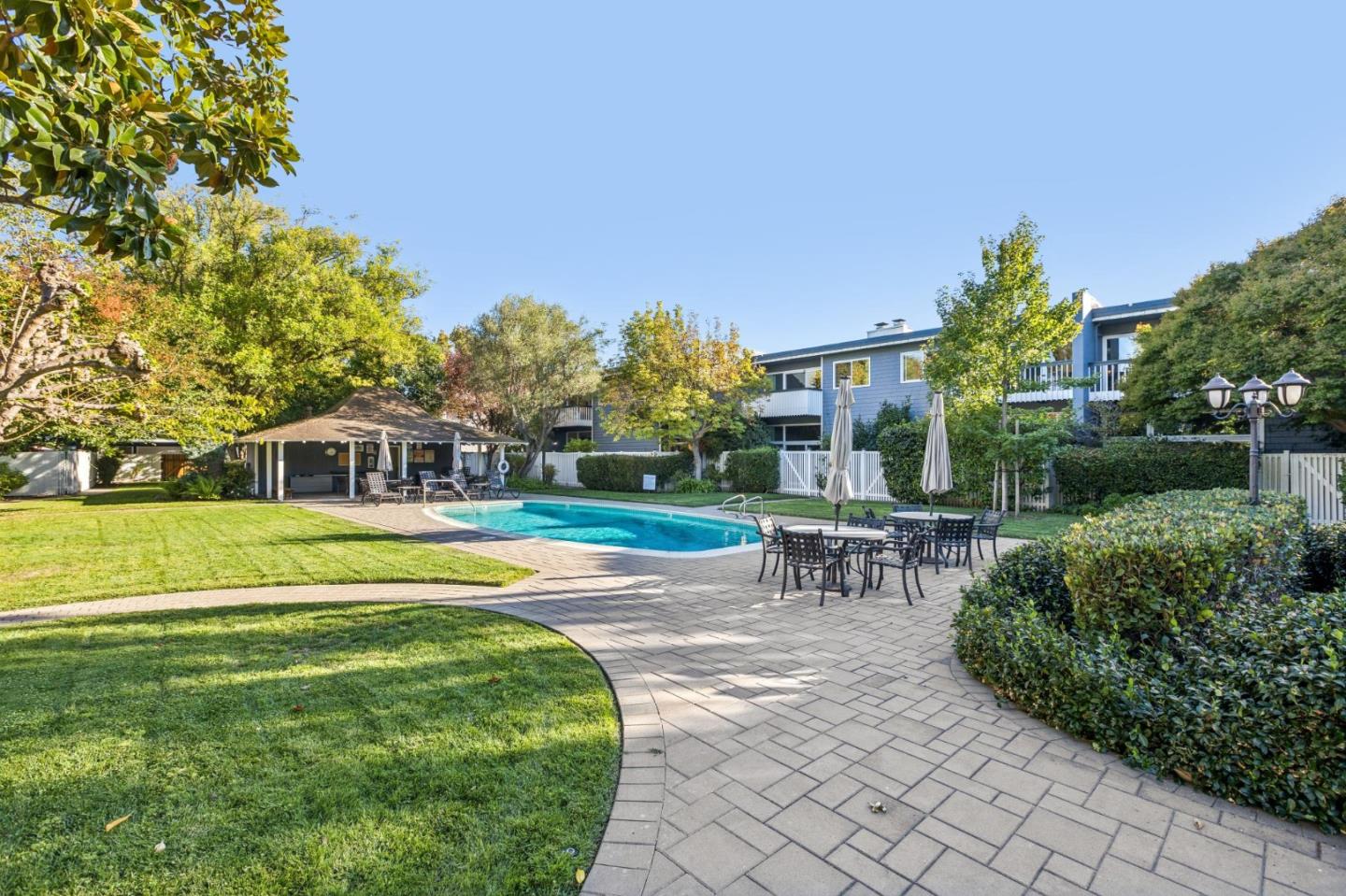 Outdoor pool courtyard with a covered pavilion, patio dining area, and landscaped lawn.
