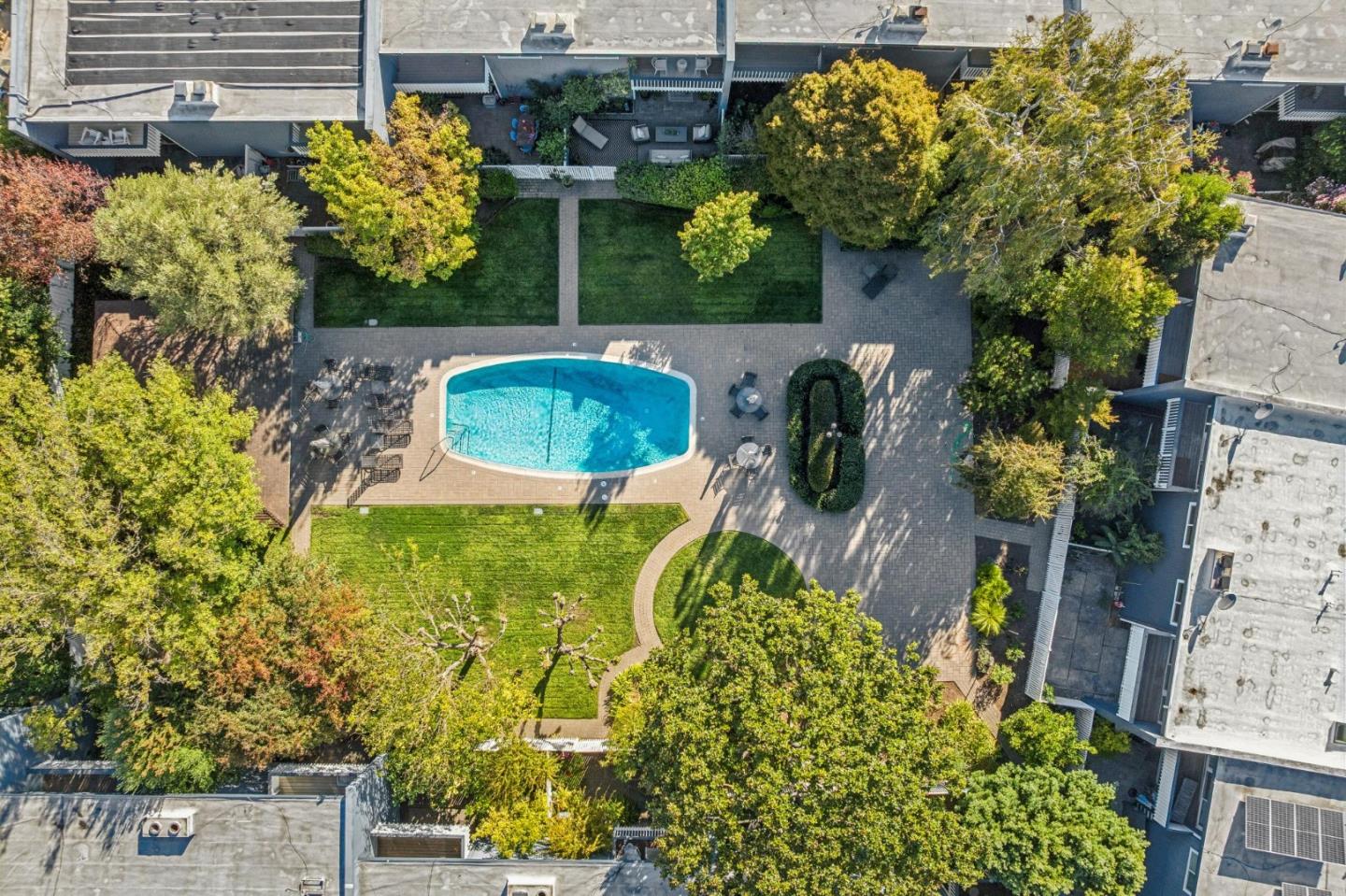 Aerial view of a courtyard pool surrounded by paved patio, lawns, and mature trees.