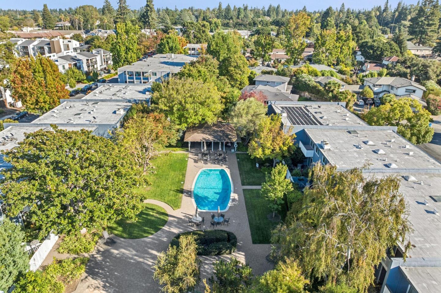 Aerial view of a residential pool and landscaped grounds surrounded by homes and mature trees.