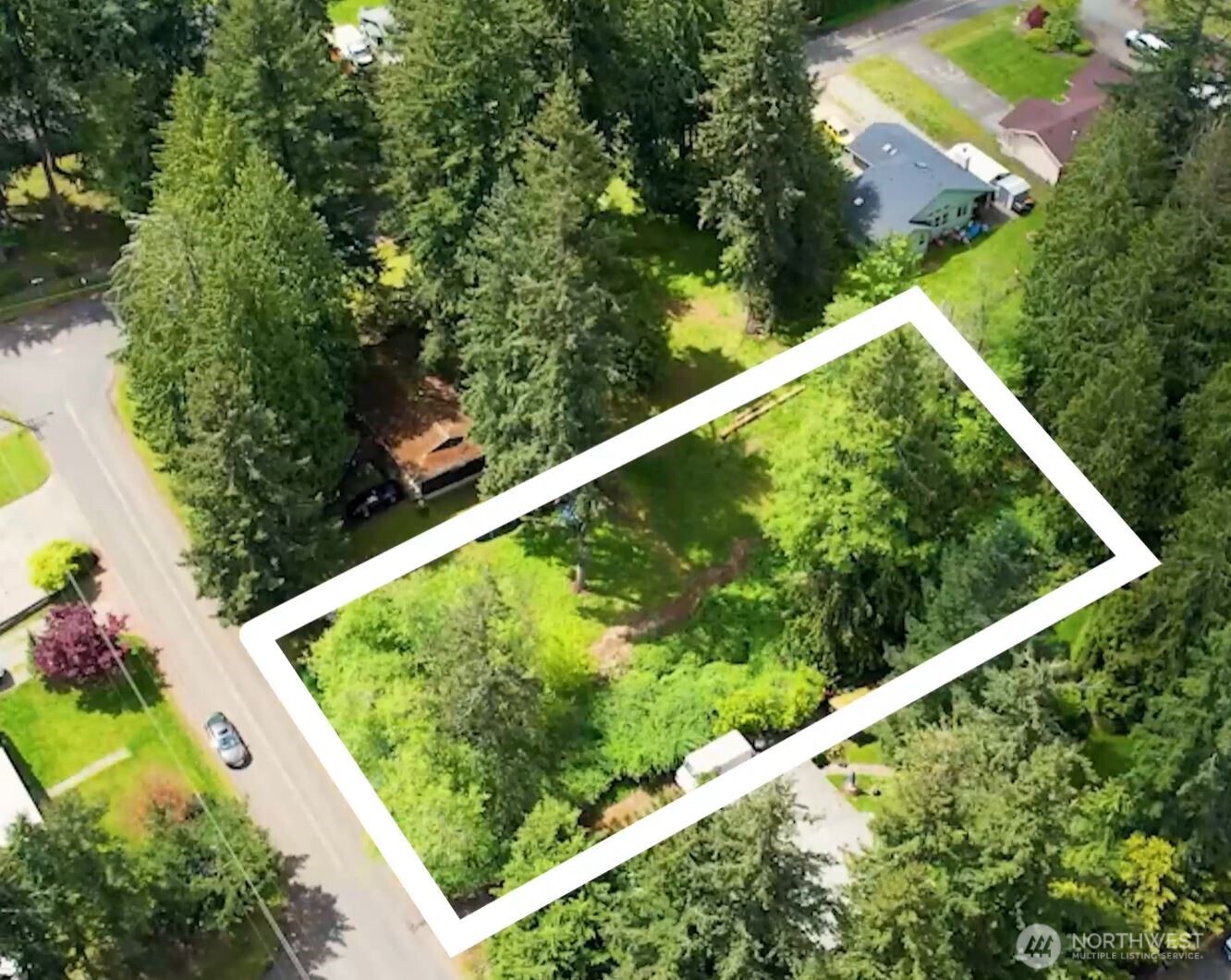 Aerial view of a wooded parcel outlined in white beside a residential street.