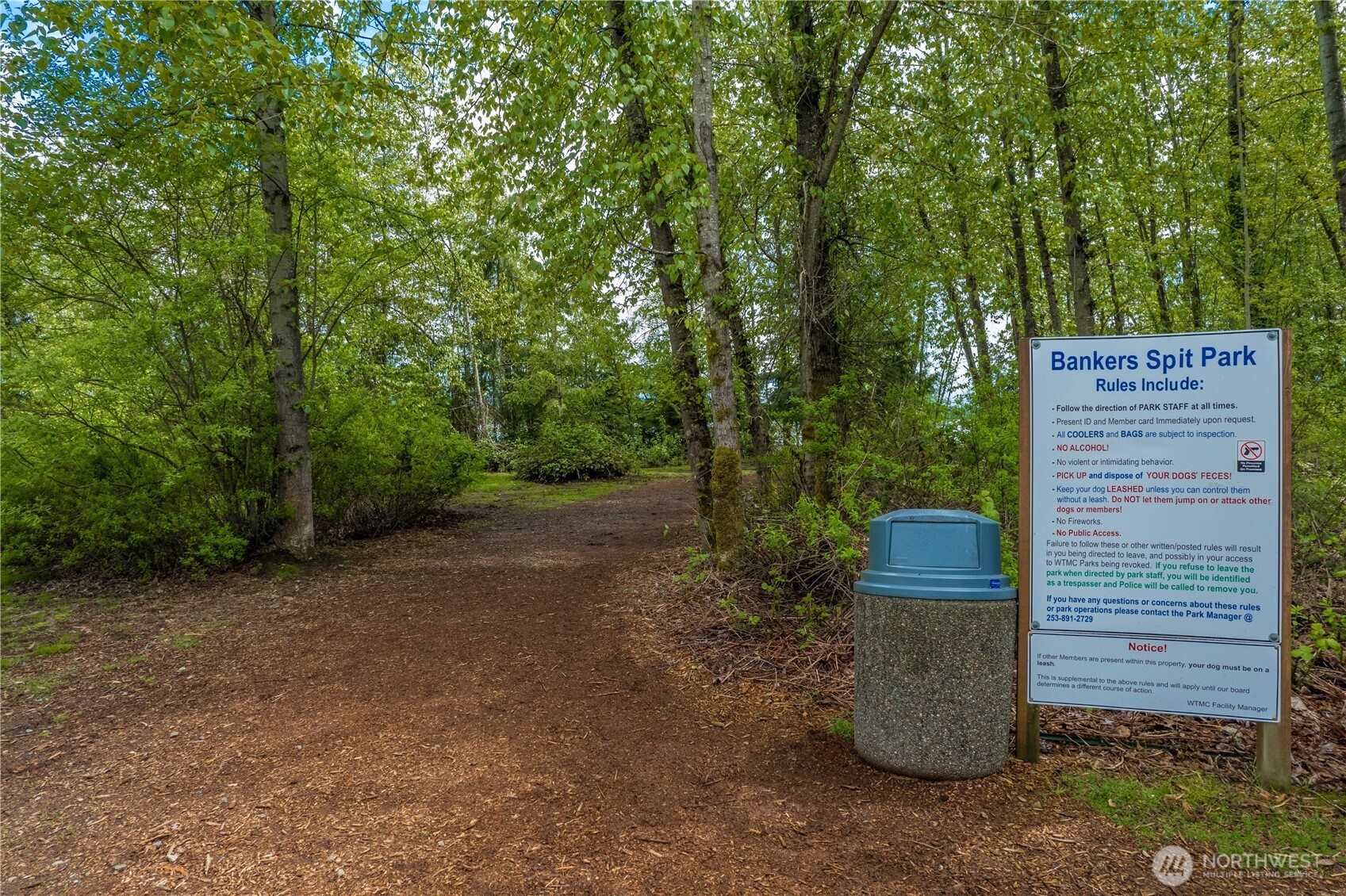 Wooded trail at Bankers Spit Park, marked by a rules sign and trash can.