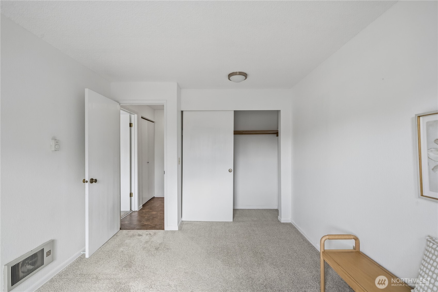Carpeted bedroom with an open closet, doorway, and small wooden chair.