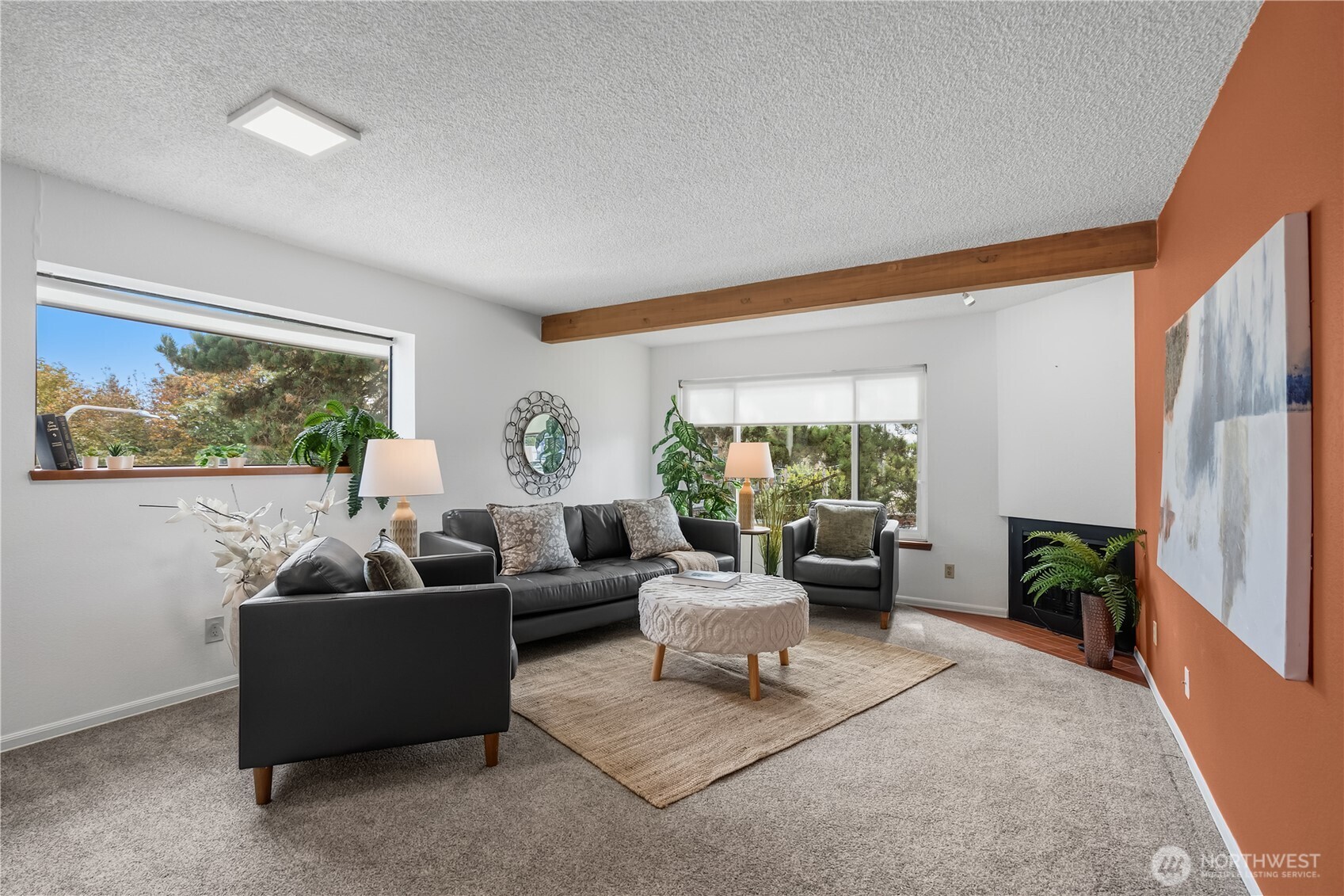 Staged living room with dark leather seating, tree-view windows, and an orange fireplace accent wall.