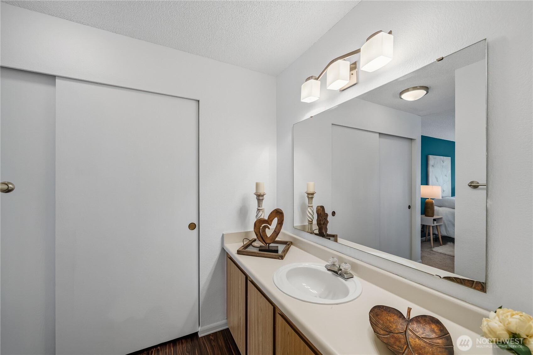 Bathroom vanity with an oval sink, large mirror, and a glimpse of a teal-accented bedroom.