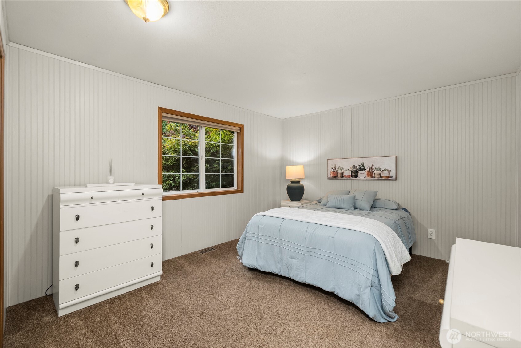 Bedroom with pale blue bedding, a white dresser, and a window overlooking greenery.