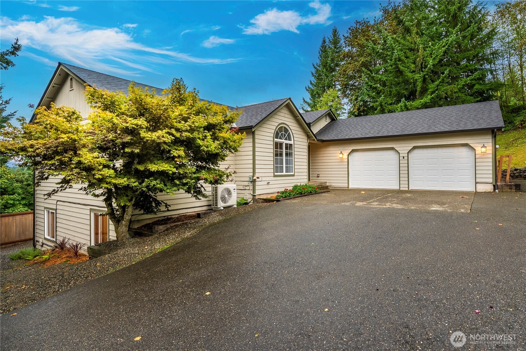 Beige house with a two-car garage and arched window beside a broad sloping driveway.