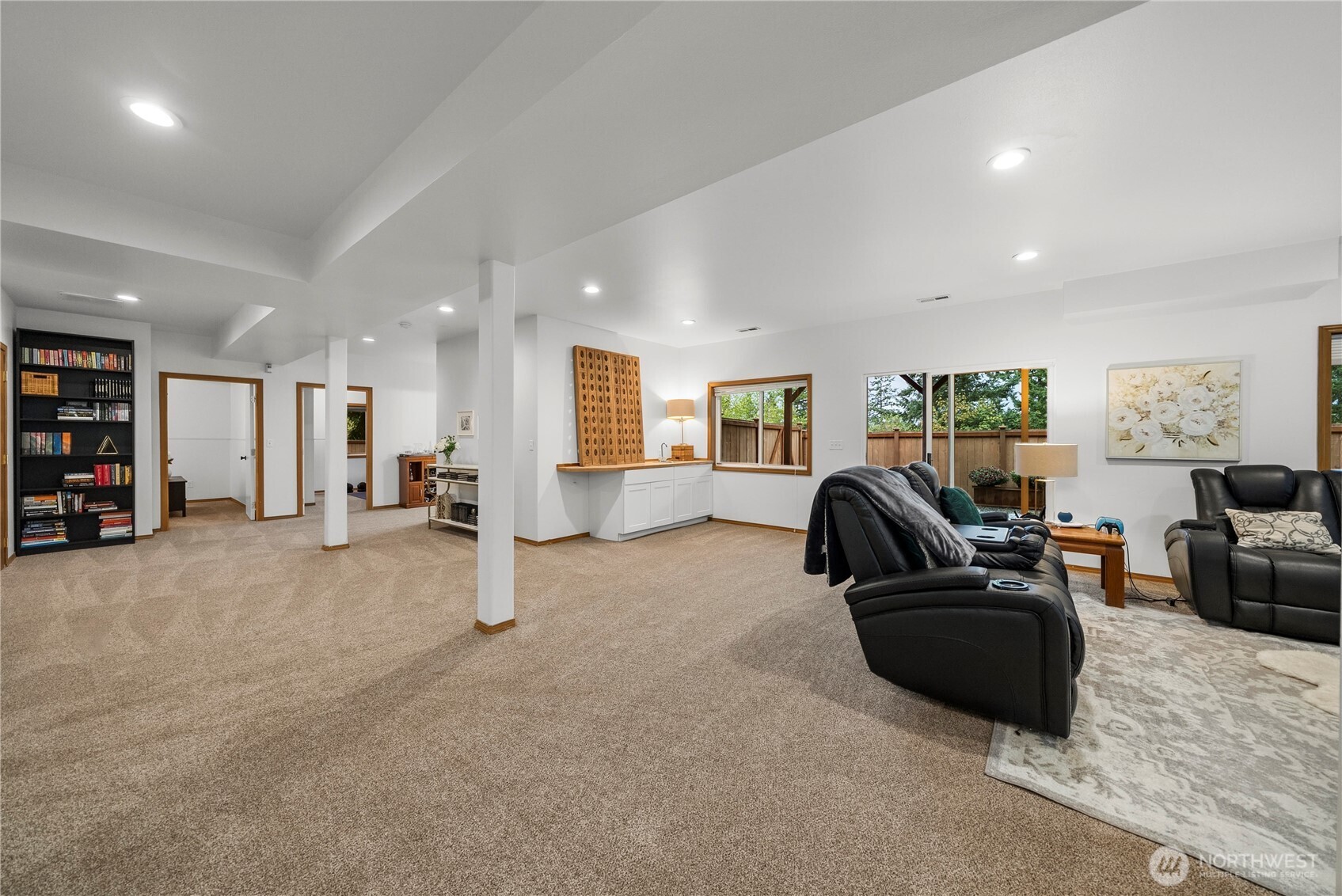 Furnished lower-level family room with black leather recliners, a white wet bar, and windows overlooking a fenced yard.