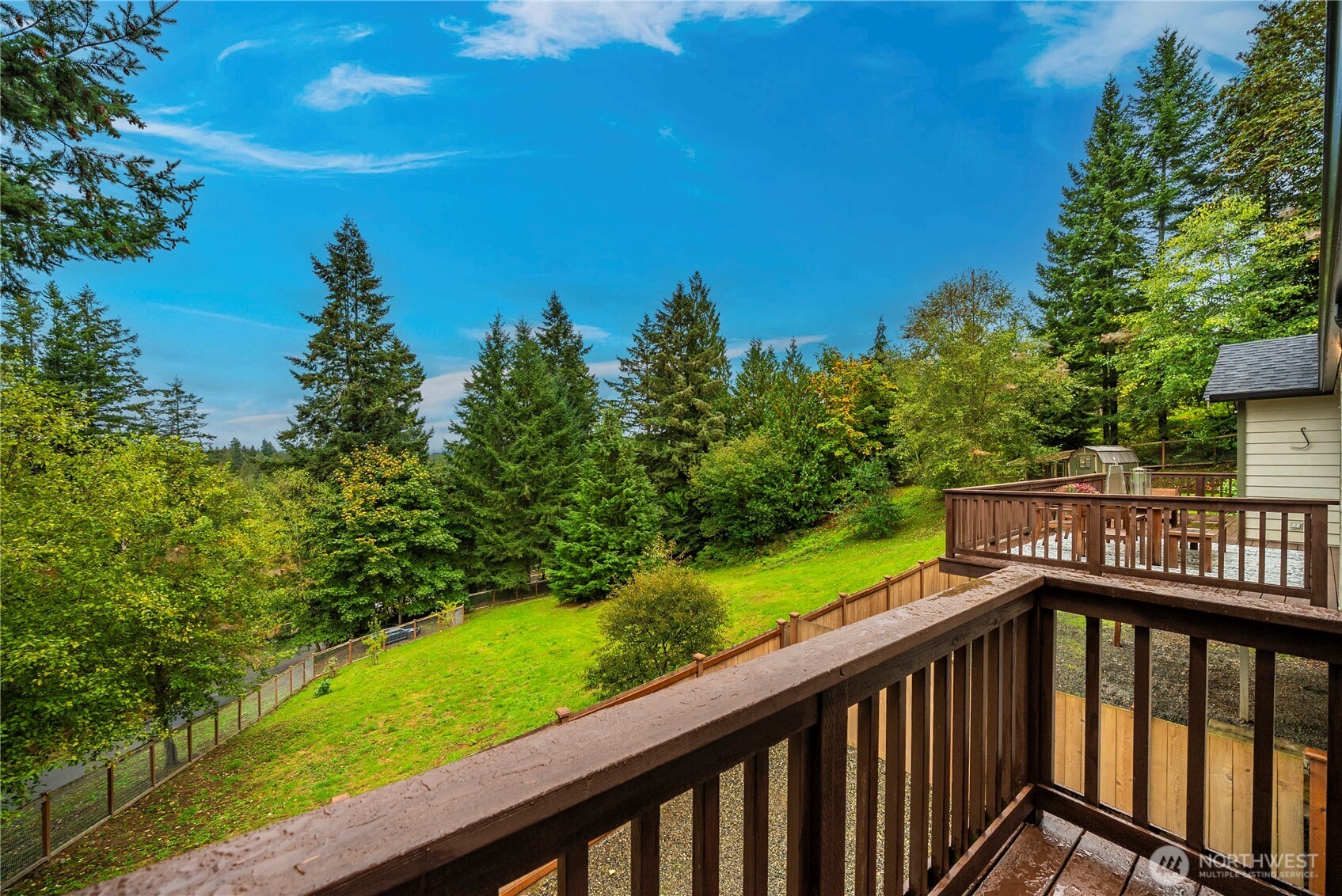 Raised wooden deck overlooking a sloping lawn and wooded property.