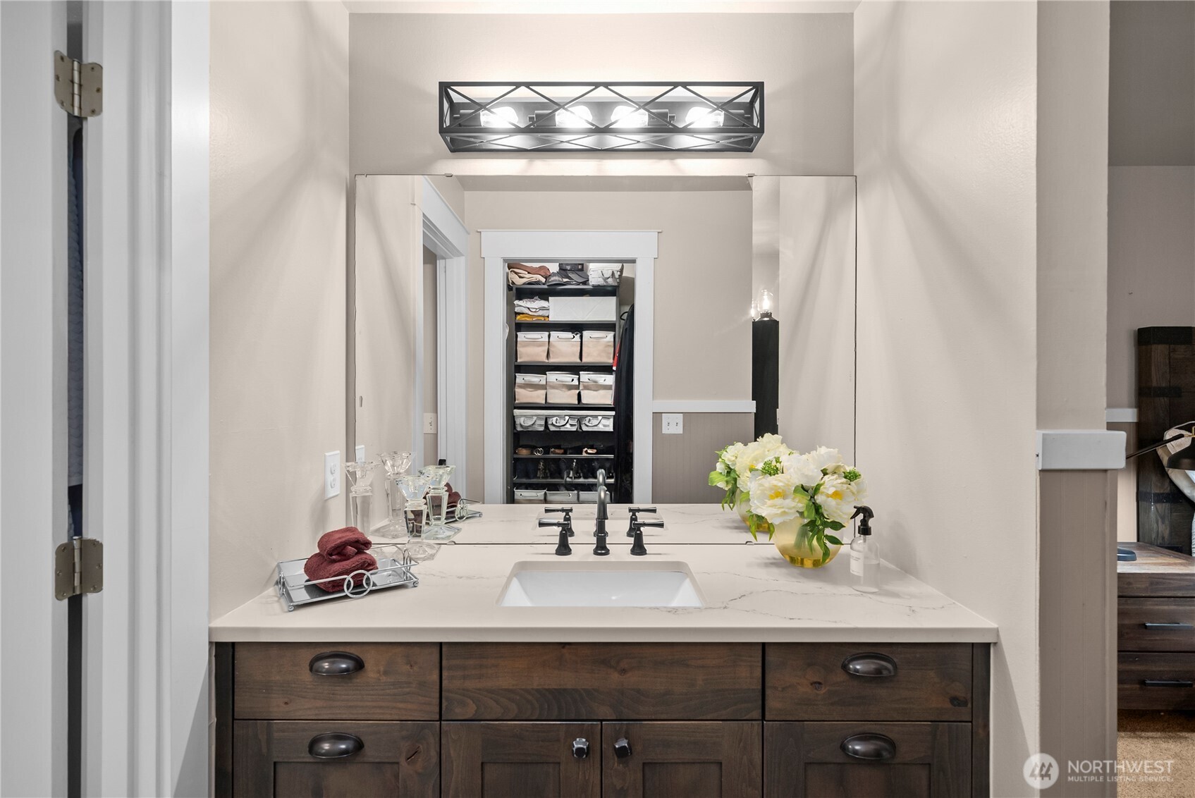 Bathroom vanity with dark wood cabinetry, a veined countertop, and a large mirror reflecting an organized closet.