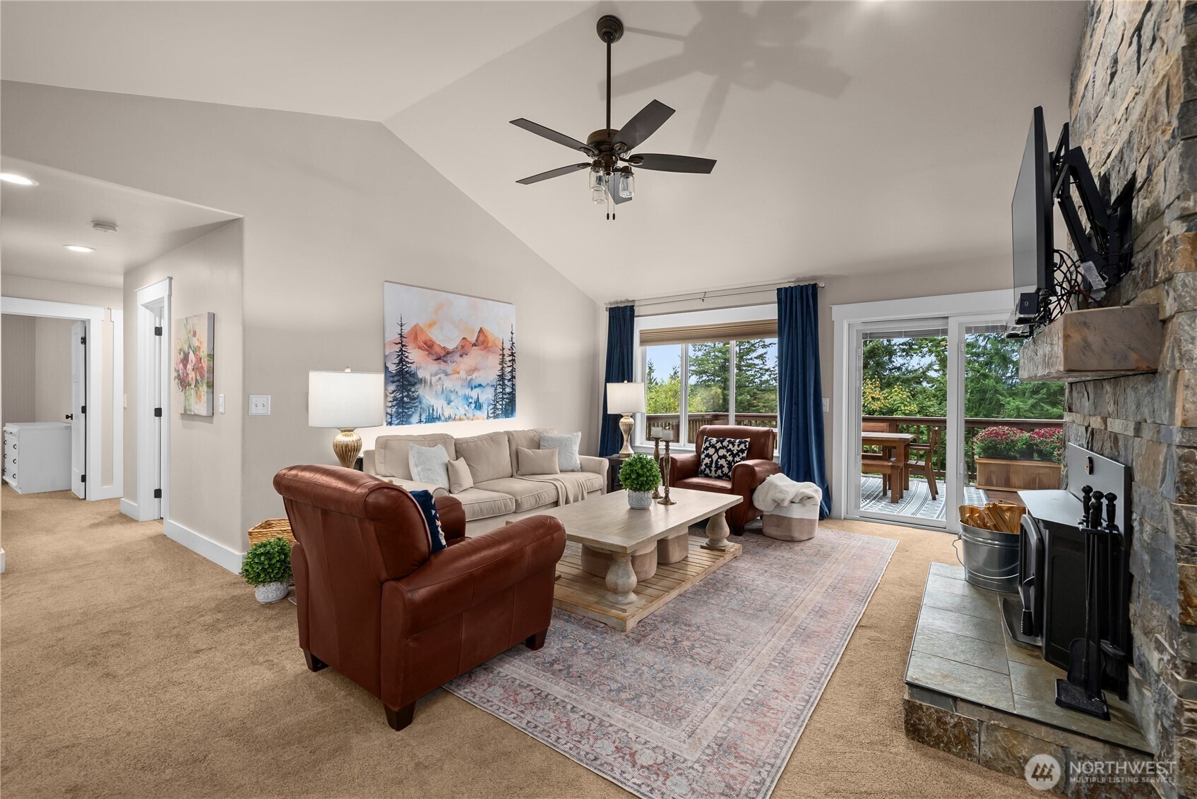 Furnished living room with a stone fireplace, vaulted ceiling, and sliding doors to a deck.