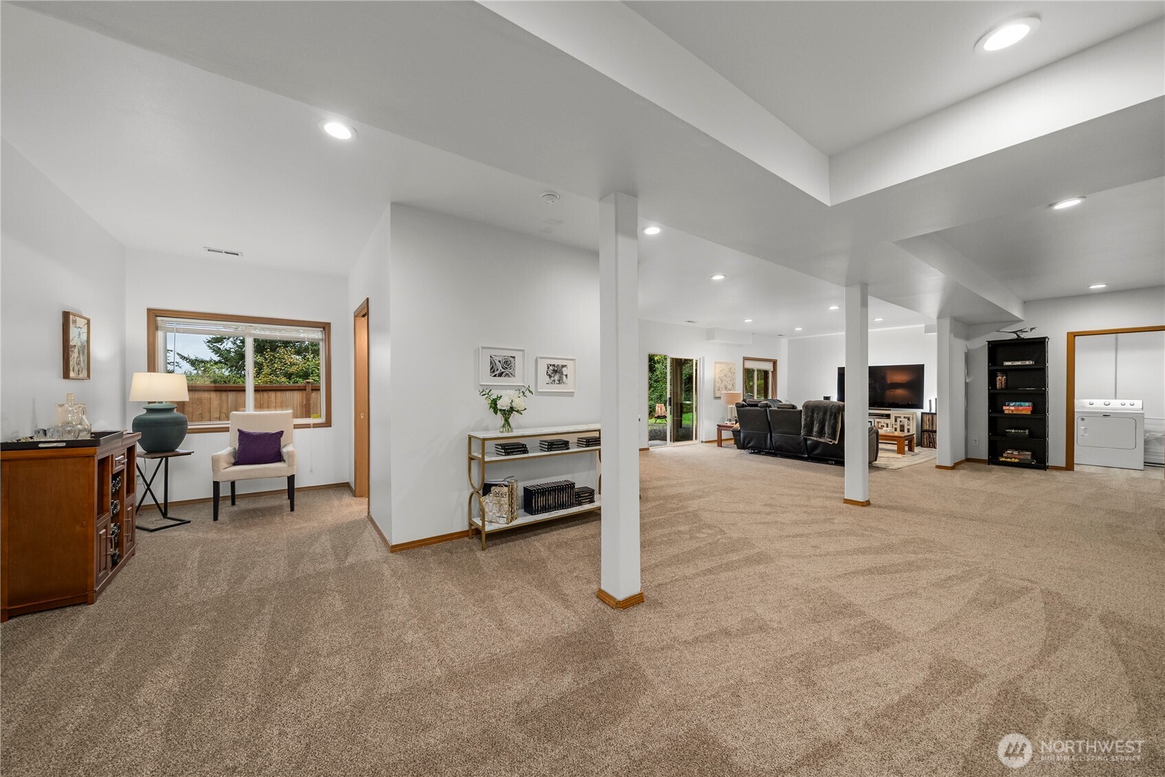 Open-plan living area with beige carpet, recliners, a television, and a laundry area.