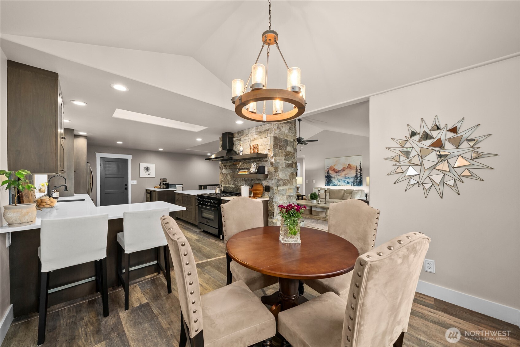 Open kitchen and dining area with a stone range hood surround and round table beneath a chandelier.