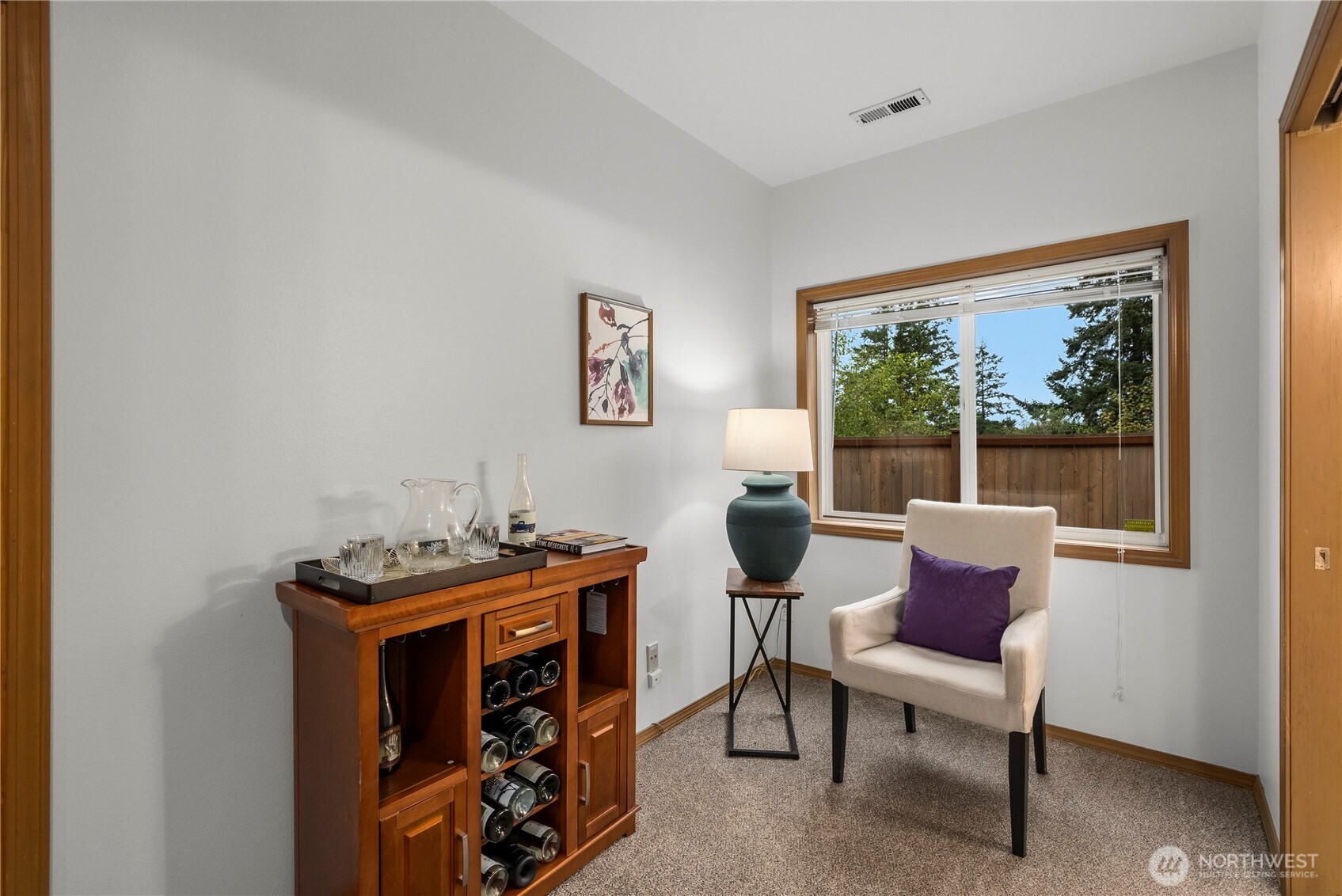 Furnished sitting nook with a wooden wine cabinet and cream armchair beside a large window.