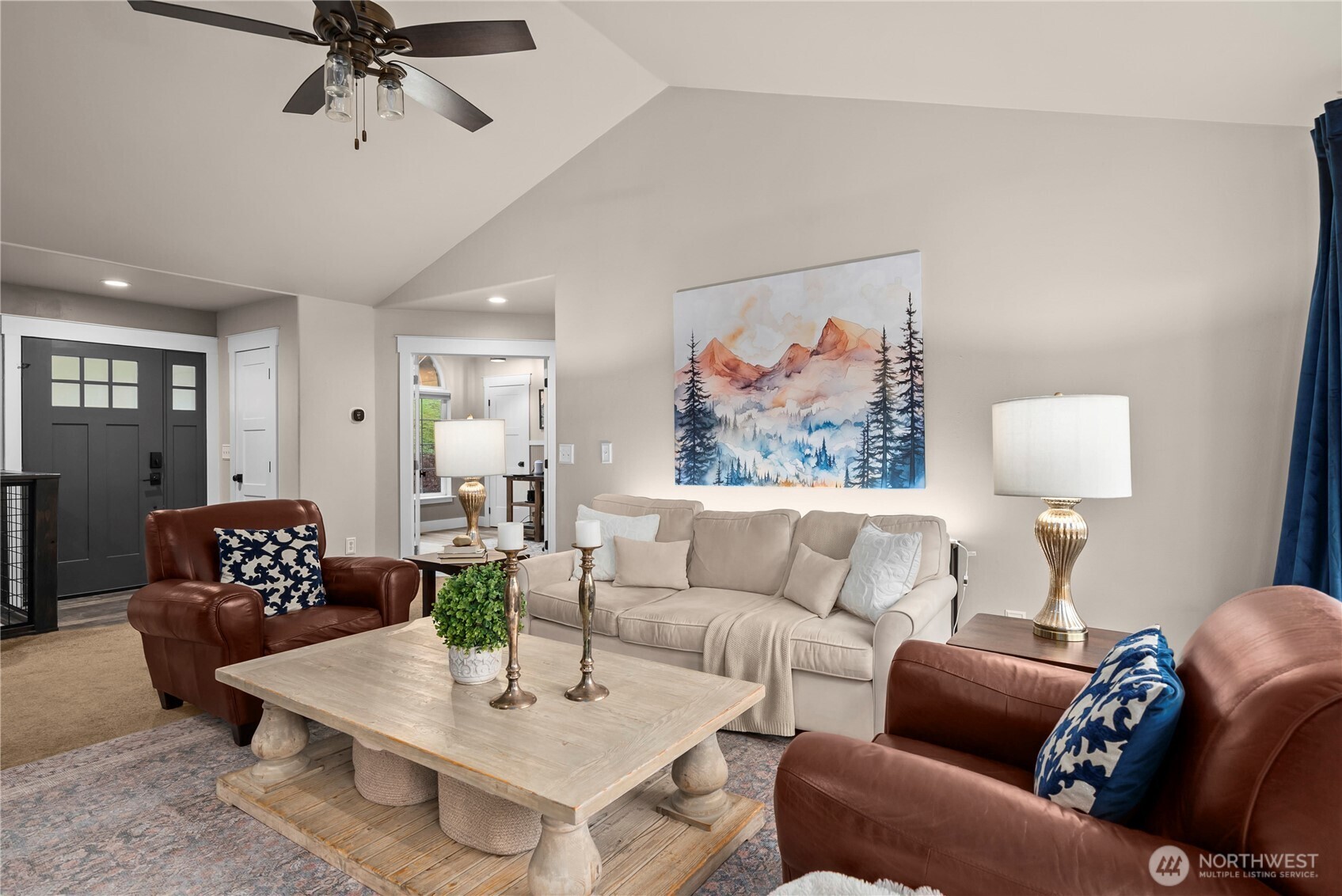 Furnished living room with a beige sofa, brown leather armchairs, and mountain artwork.