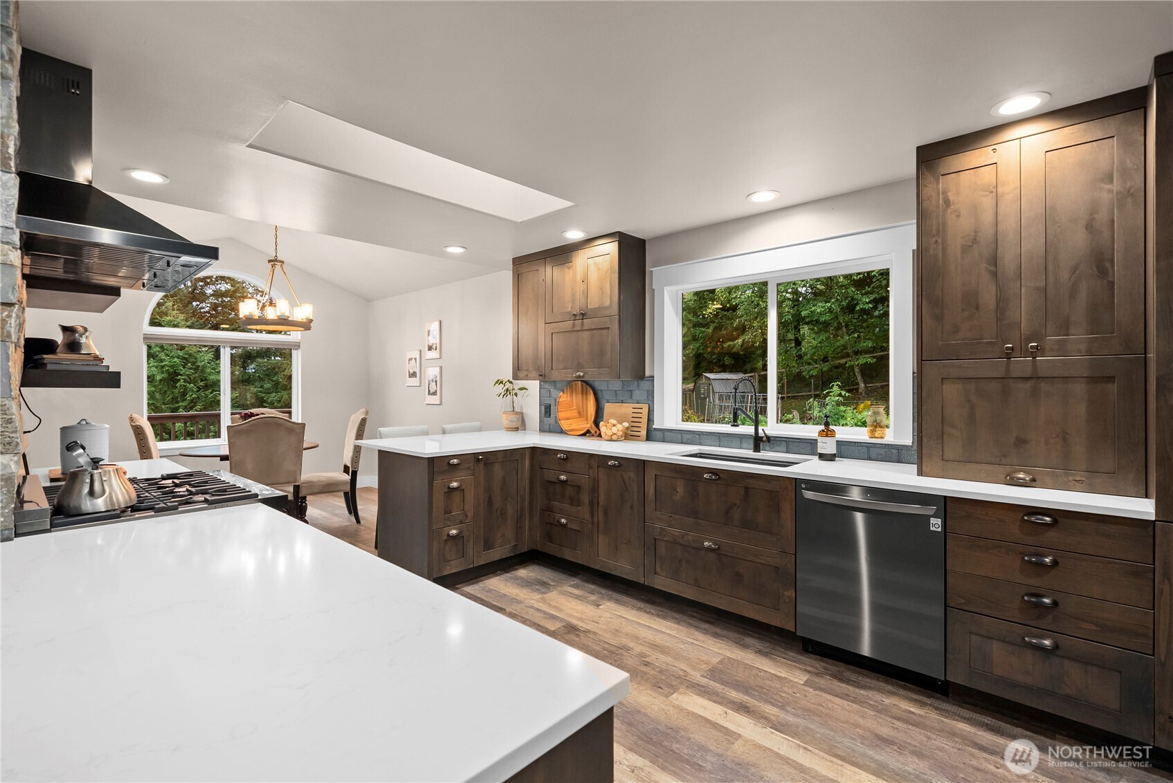 Kitchen with dark wood cabinetry, white countertops, a large island, and a window overlooking trees.