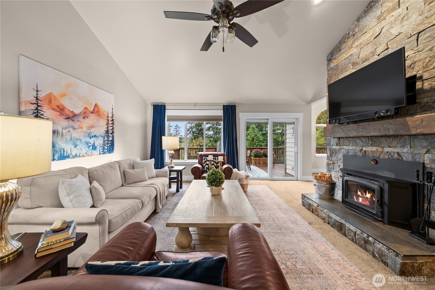 Living room with a vaulted ceiling, stone fireplace, and sliding doors to a deck.