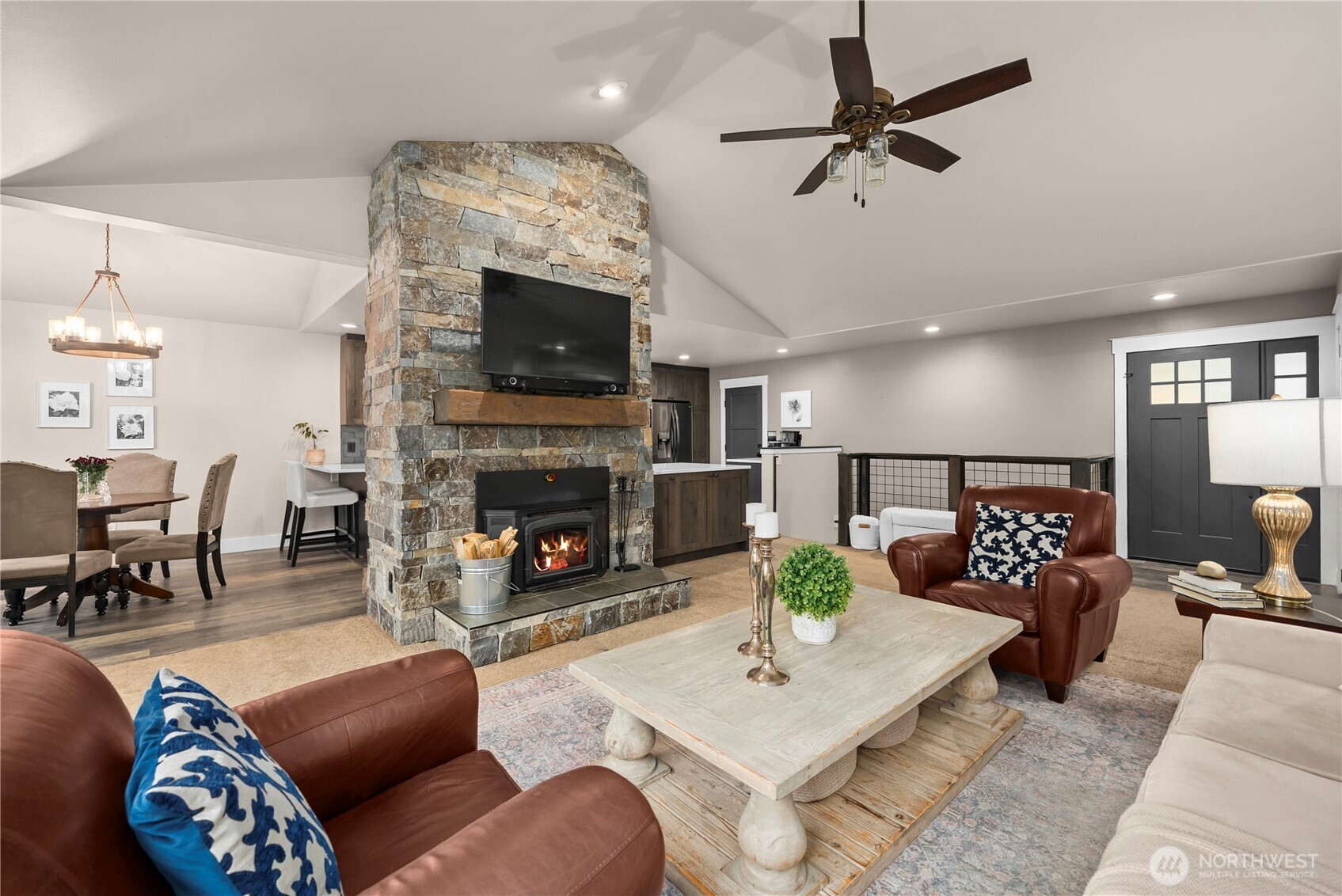 Living room with a tall stone fireplace, vaulted ceiling, and leather seating.