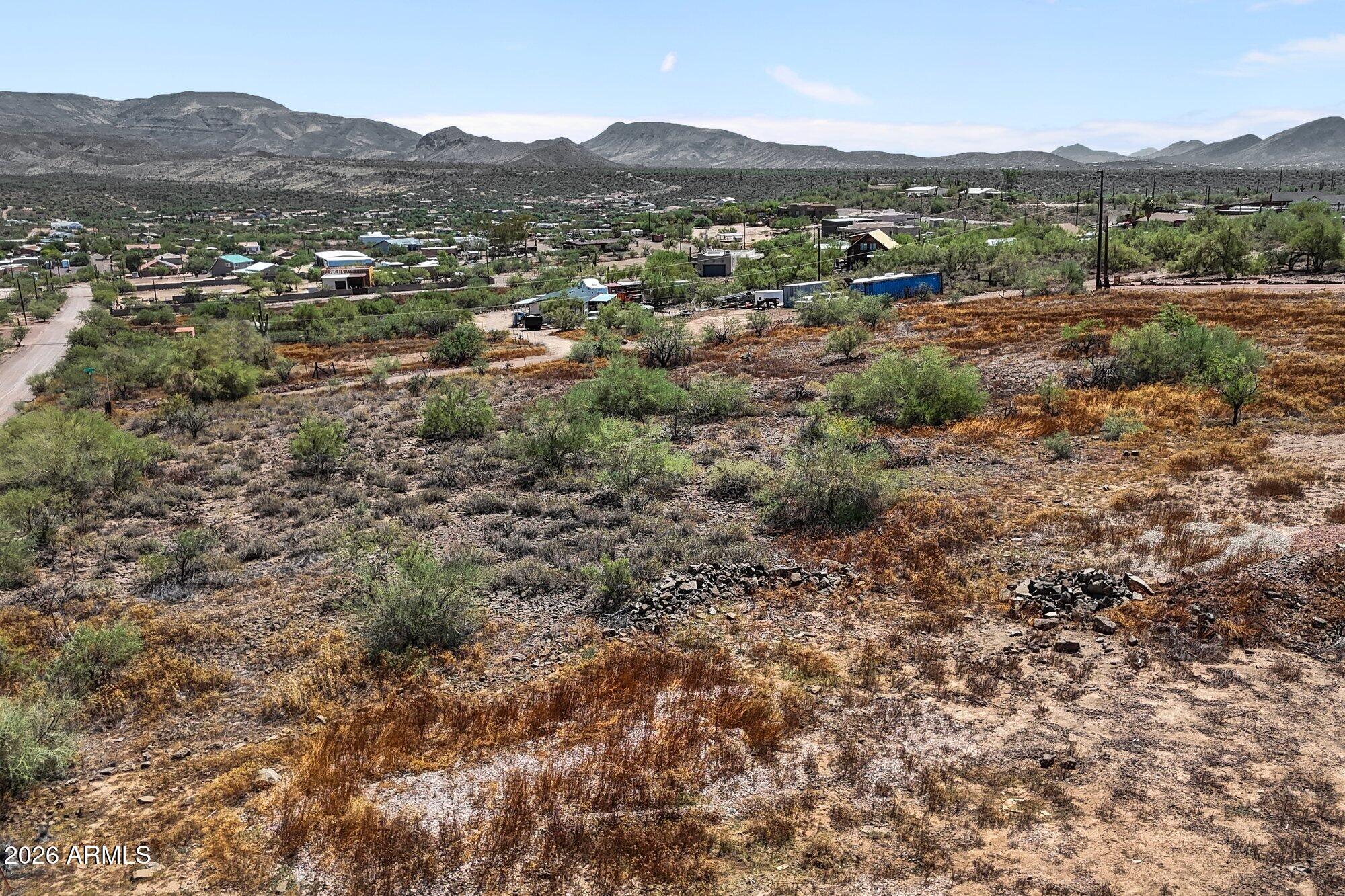 Rocky desert parcel with sparse shrubs, scattered homes, and mountains in the distance.