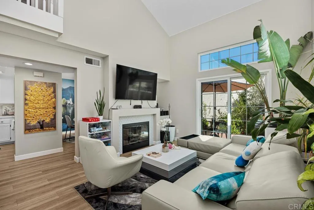 Furnished living room with vaulted ceilings, fireplace, large sectional, and garden-facing sliding glass doors.