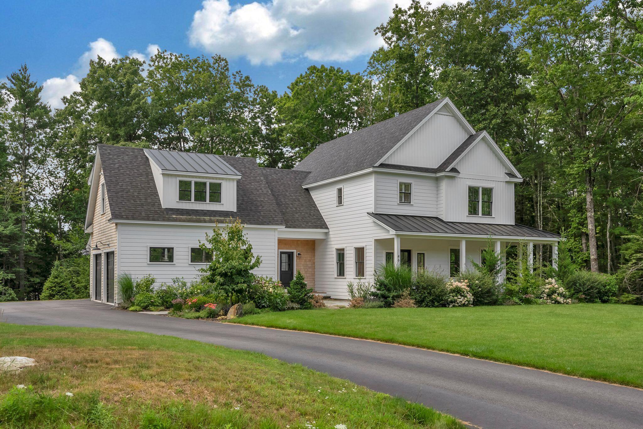 White two-story home with a covered porch, landscaped gardens, and mature trees.