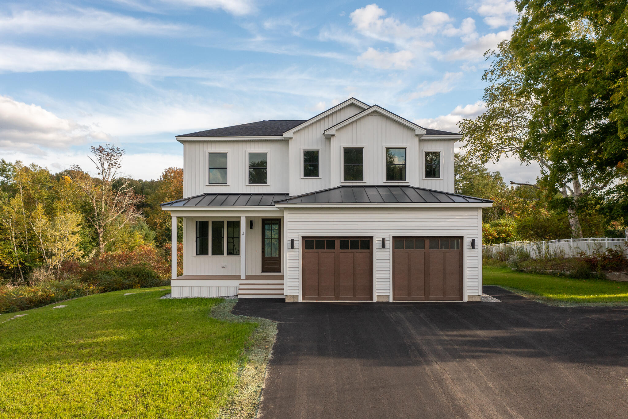 Two-story white house with a covered porch, dark metal roof accents, and a two-car garage.