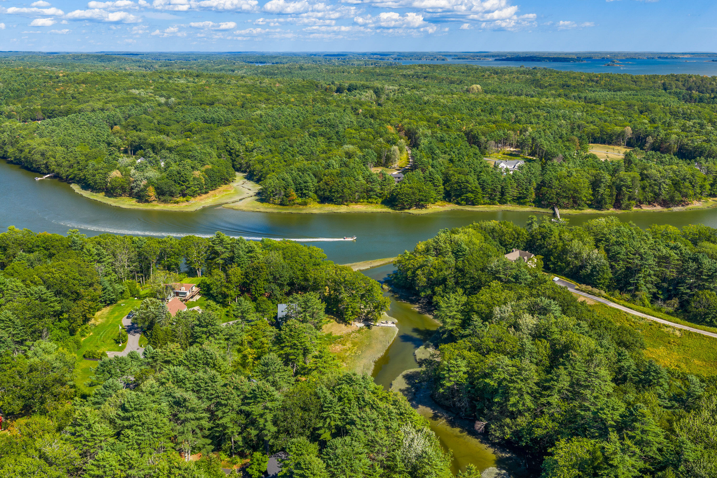 Aerial view of a winding river through wooded coastal Yarmouth, with scattered homes and water in the distance.