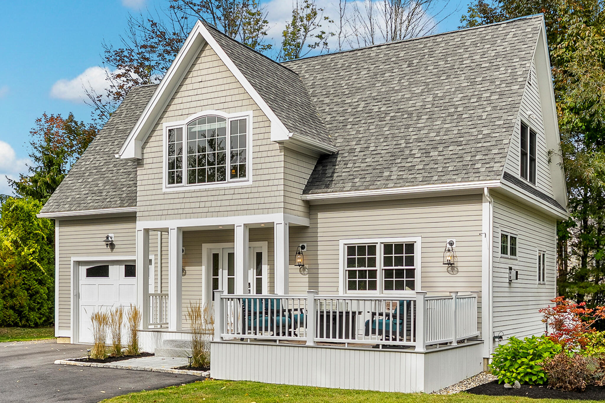 Light gray two-story home with a steep gabled roof, arched upper window, garage, and covered porch.
