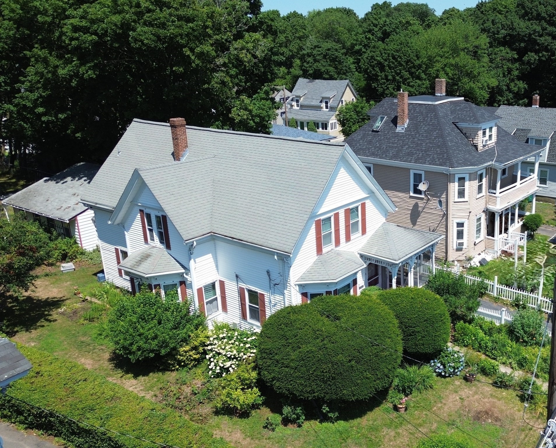 Aerial view of a white multi-story house with red shutters and landscaped grounds.