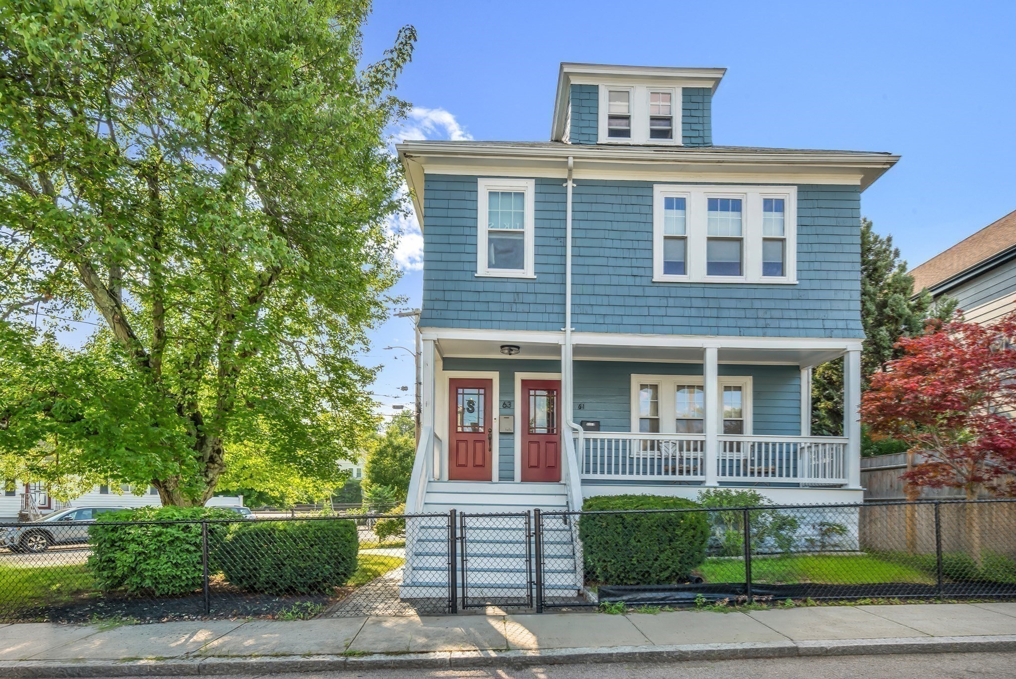 Blue-shingled multi-unit home with a white-railed porch, red entry doors, and fenced yard.