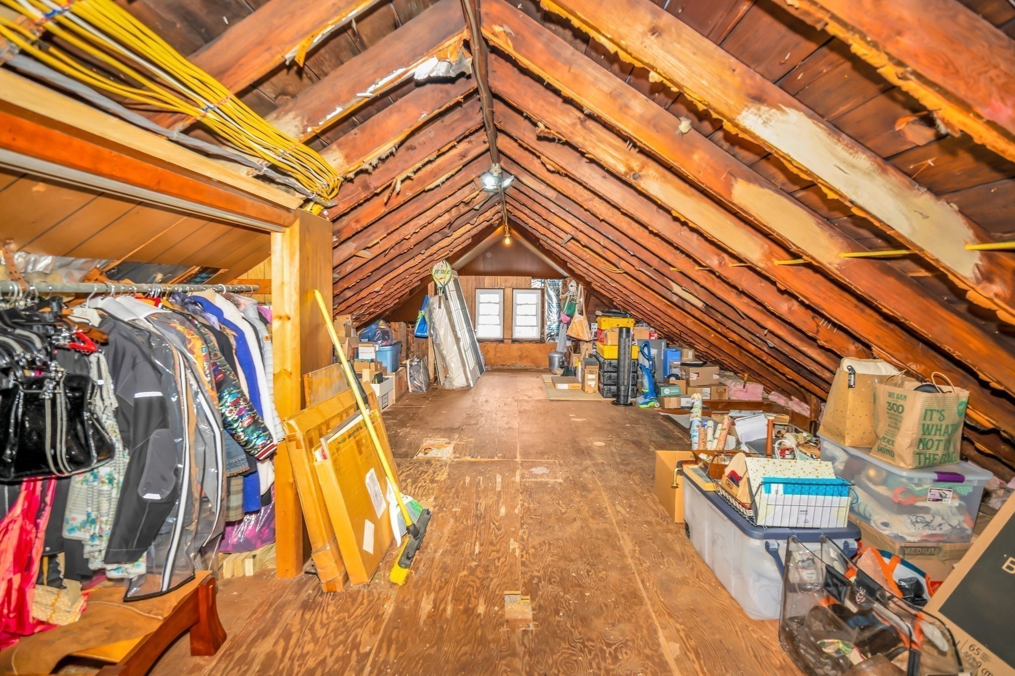 Attic storage space with exposed rafters, hanging clothes, bins, and boxes.