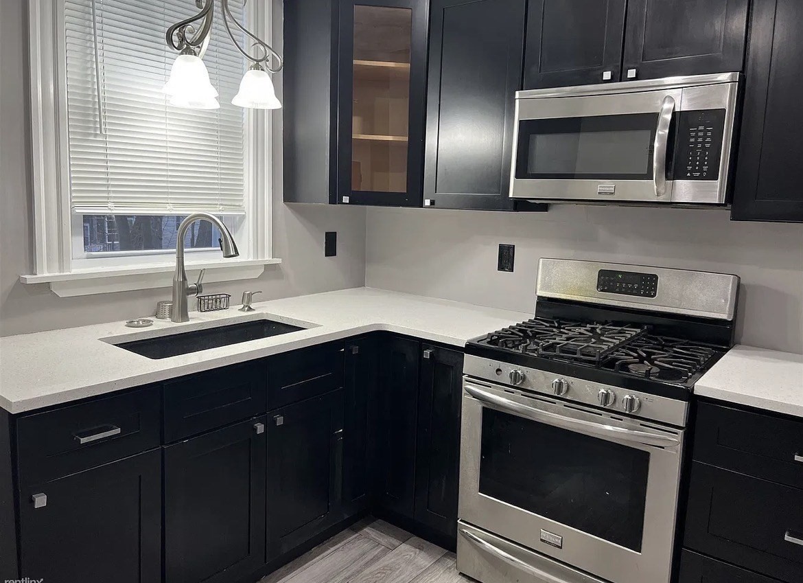 Kitchen with navy cabinets, white counters, stainless appliances, and a sink beneath a window.