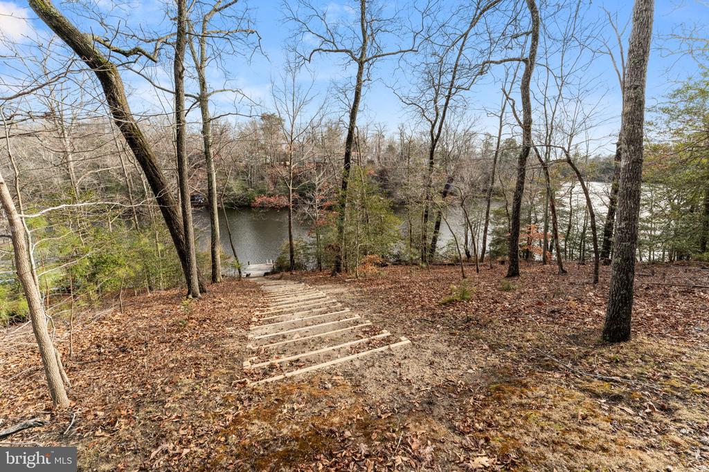 Wooded backyard slopes down via timber steps to a calm waterfront.