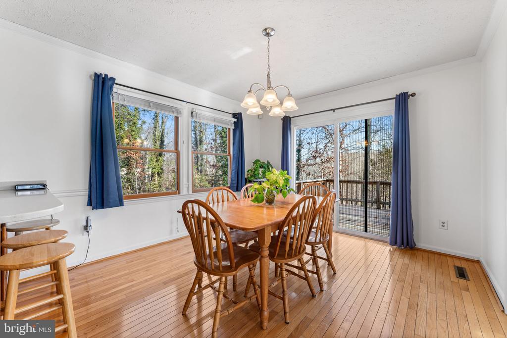 Dining room with a wooden table, hardwood floors, and blue-curtained windows overlooking a deck.