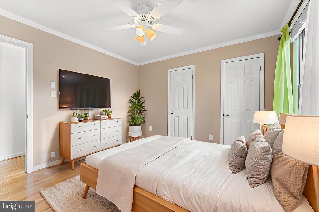 Bedroom with white bedding, a wall-mounted TV, ceiling fan, and bright green curtains.