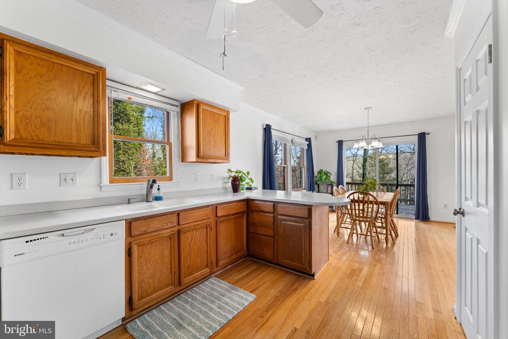 Kitchen with warm wood cabinets and hardwood floors opening to a dining area with large windows.