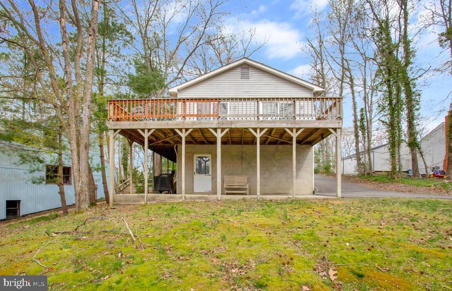 Raised house with a large elevated wooden deck on a wooded lot.