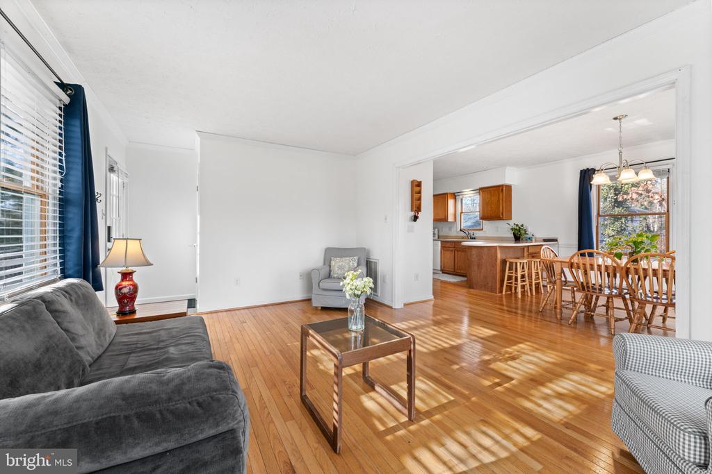 Living room opening to a dining area and kitchen, with hardwood floors and large windows.