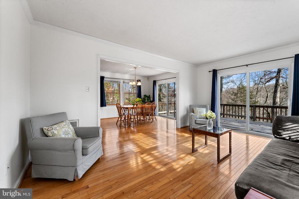Living room with hardwood floors, opening to a dining area and deck overlooking trees.