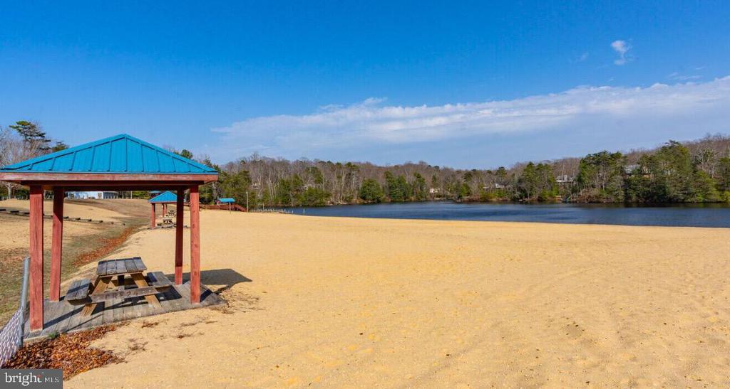 Sandy beach with a blue-roofed picnic pavilion beside a wooded lake.