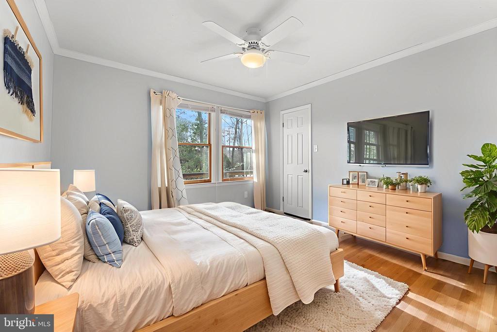 Bedroom with a large bed, hardwood floors, and a window overlooking trees.